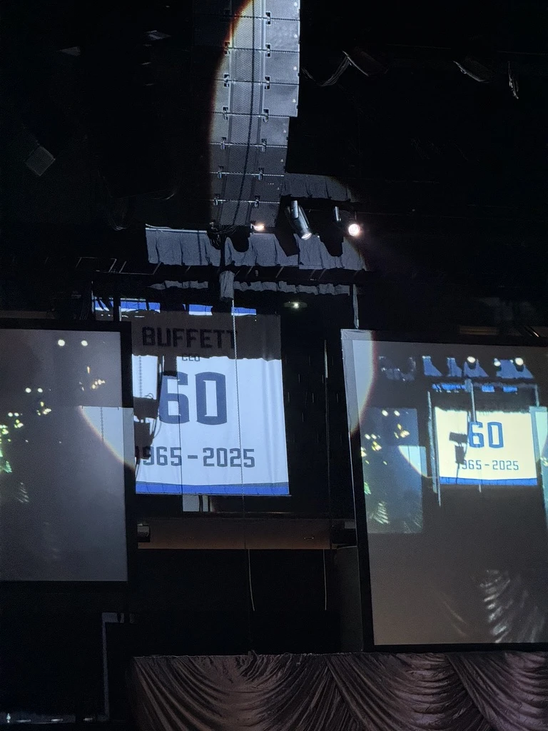 A white Warren Buffett tribute banner hangs between projection screens inside the arena.