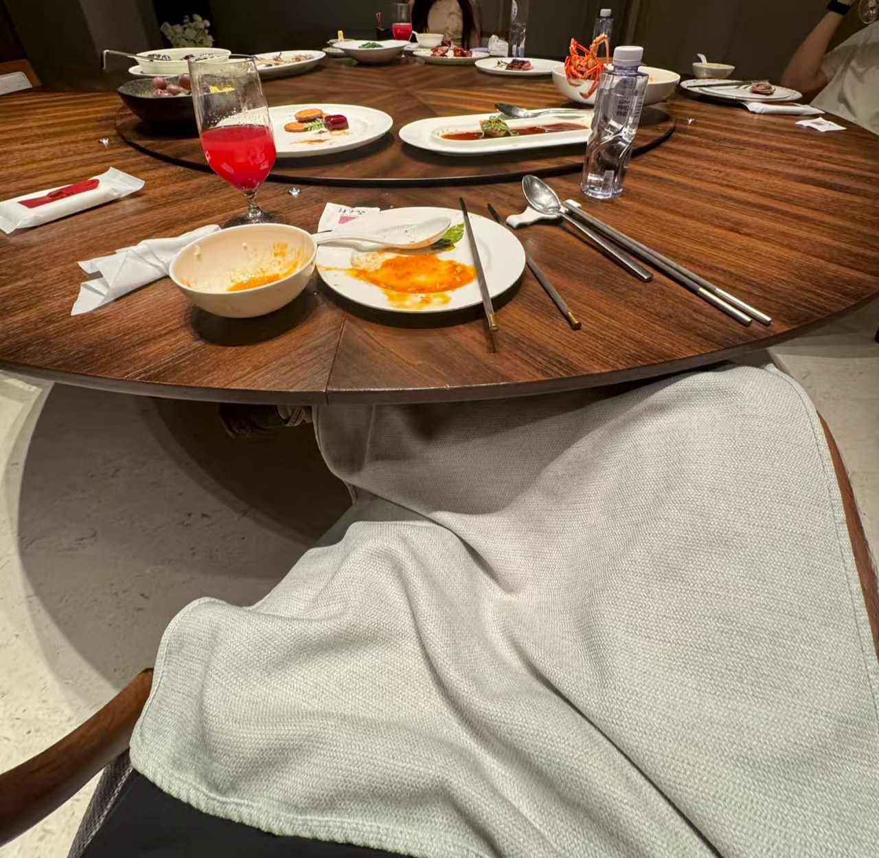 A large round restaurant table after dinner, with nearly finished dishes, chopsticks, spoons, and a red drink still in place.