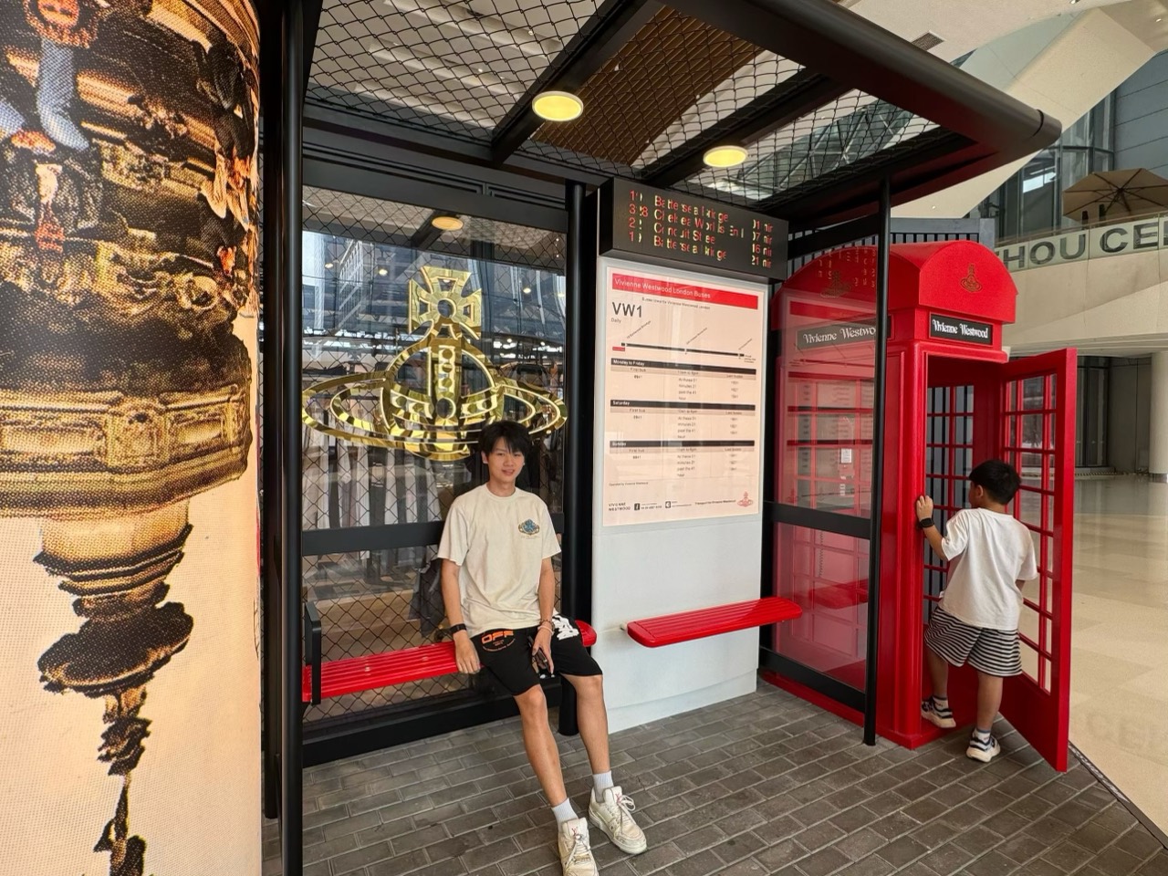A friend sits at a Vivienne Westwood-themed bus-stop display beside a bright red British telephone box.